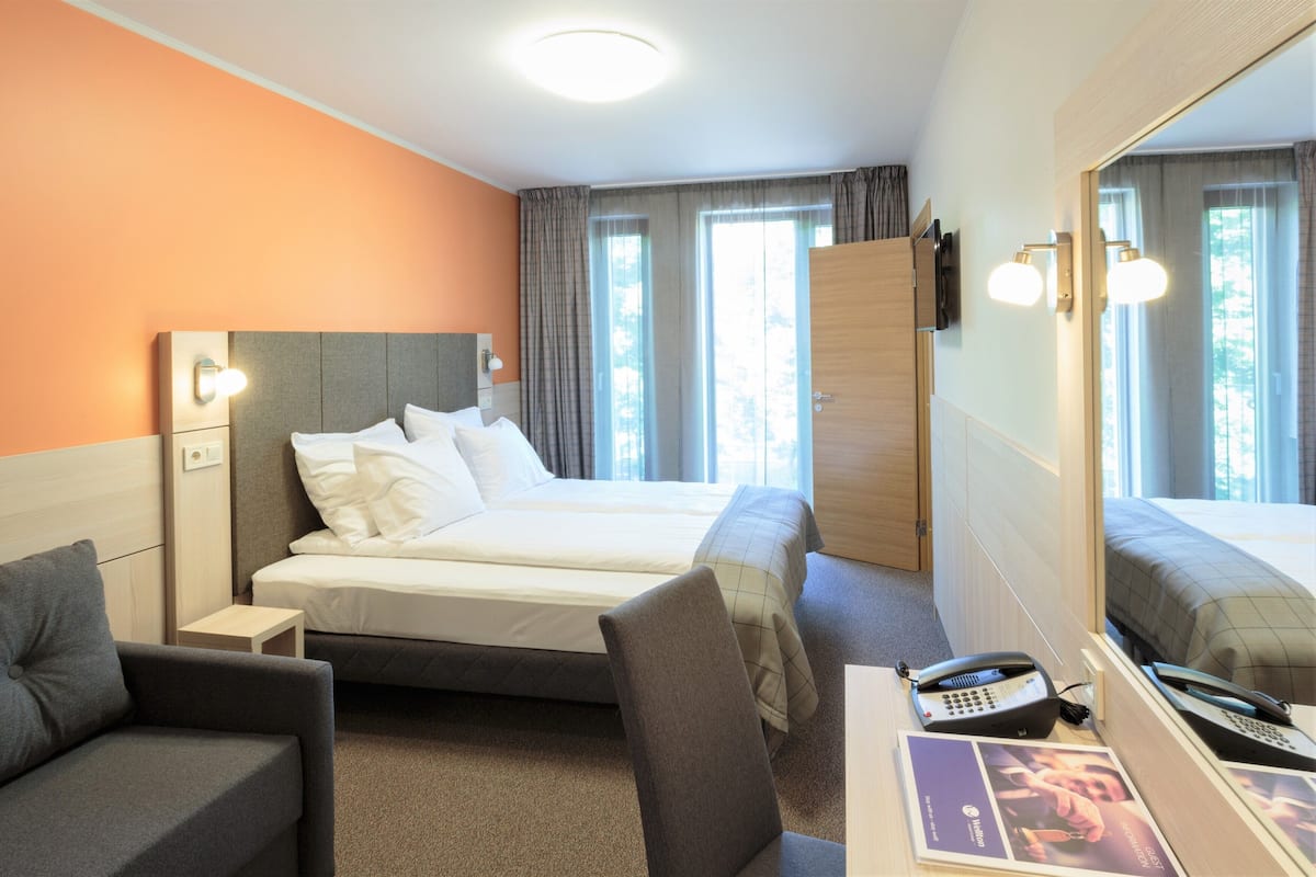 Habitación de hotel con una cama, un escritorio con teléfono, una silla, una mesita y un espejo grande.