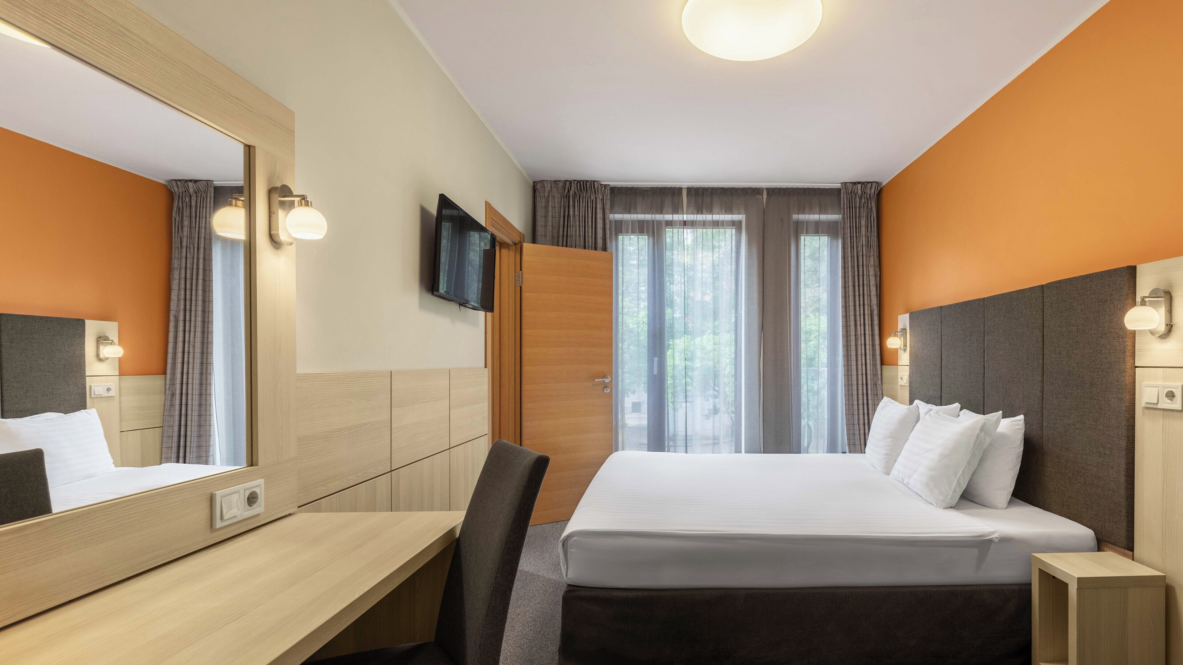 A hotel room with a bed, a desk, a chair, a TV, and a wardrobe.