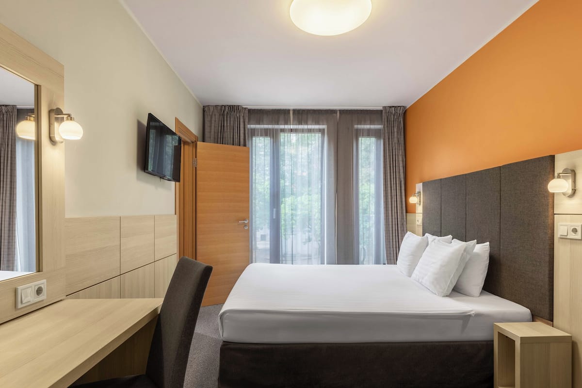 A hotel room with a bed, a desk, a chair, a TV, and a wardrobe.