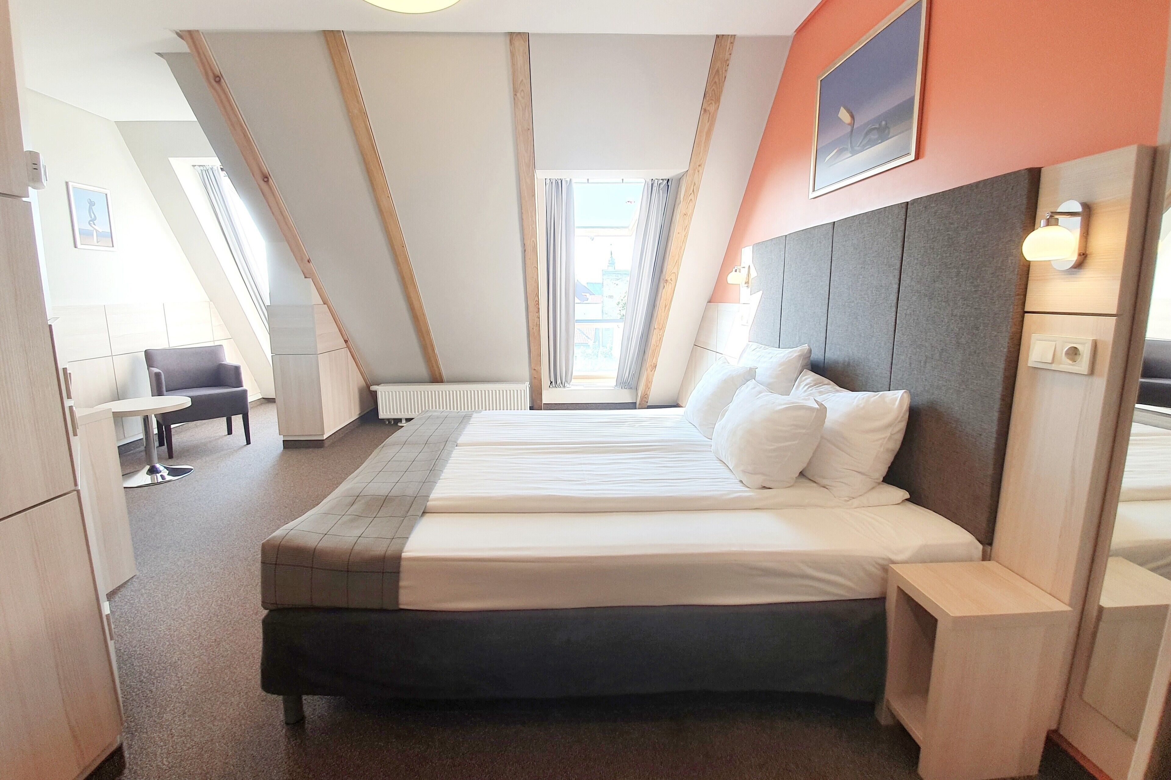 Habitación de hotel moderna con una cama grande, un escritorio y vistas de la ciudad a través de un ventanal amplio.