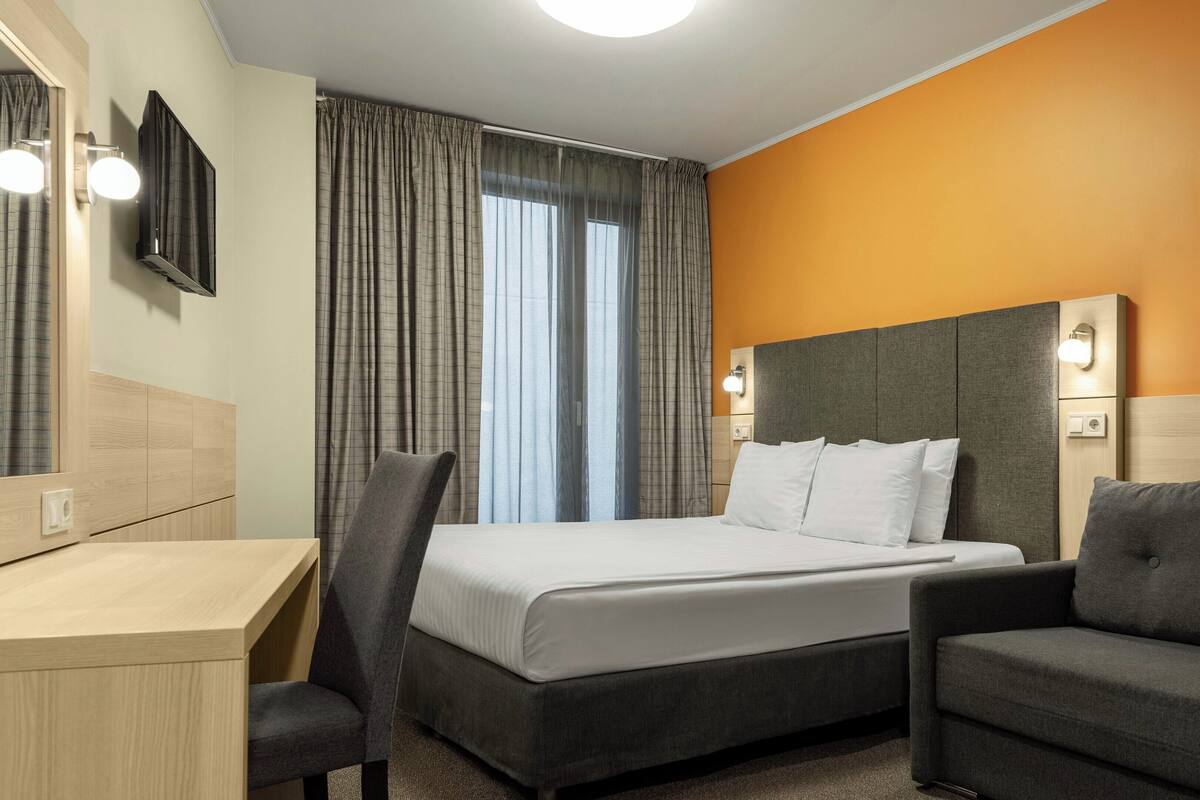 Una habitación de hotel con una cama, un escritorio, una silla, un sofá y un cuadro en la pared.