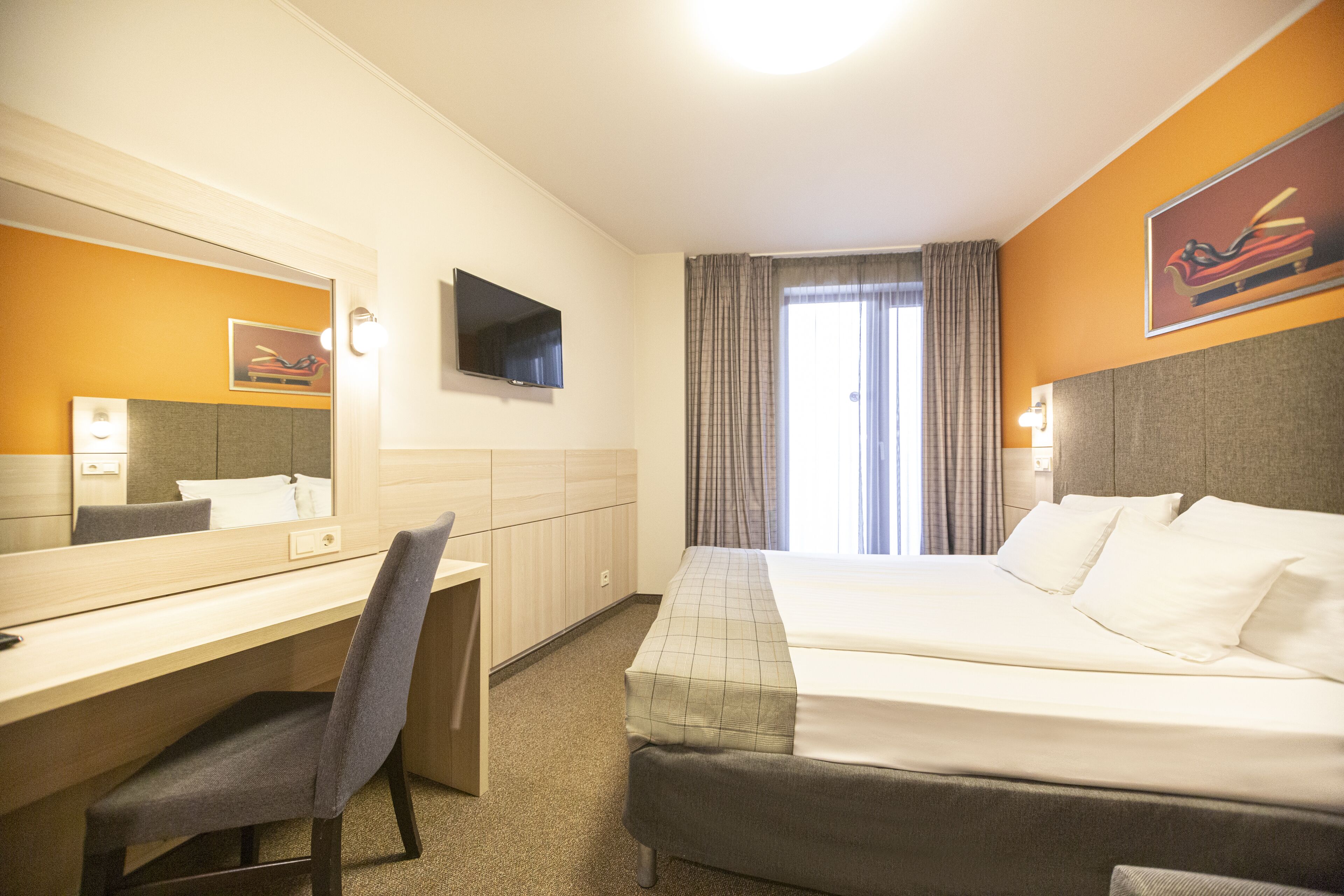 Una camera d'albergo con un letto, una scrivania, una sedia, una televisione e una finestra con tende.