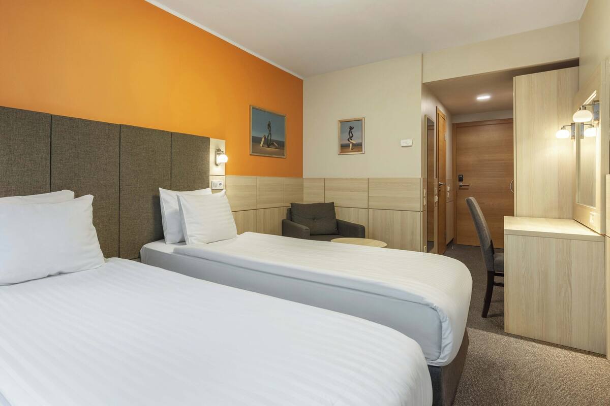 Una habitación de hotel con dos camas, un escritorio, una silla y un armario.
