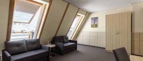 A modern loft bedroom with a sloped ceiling, skylights, a sofa, a chair, and a small table.