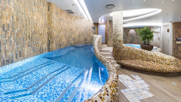 A modern indoor swimming pool with mosaic tiling, a curved seating area, and a potted plant. - Wellton Riga Hotel & SPA (Riga)