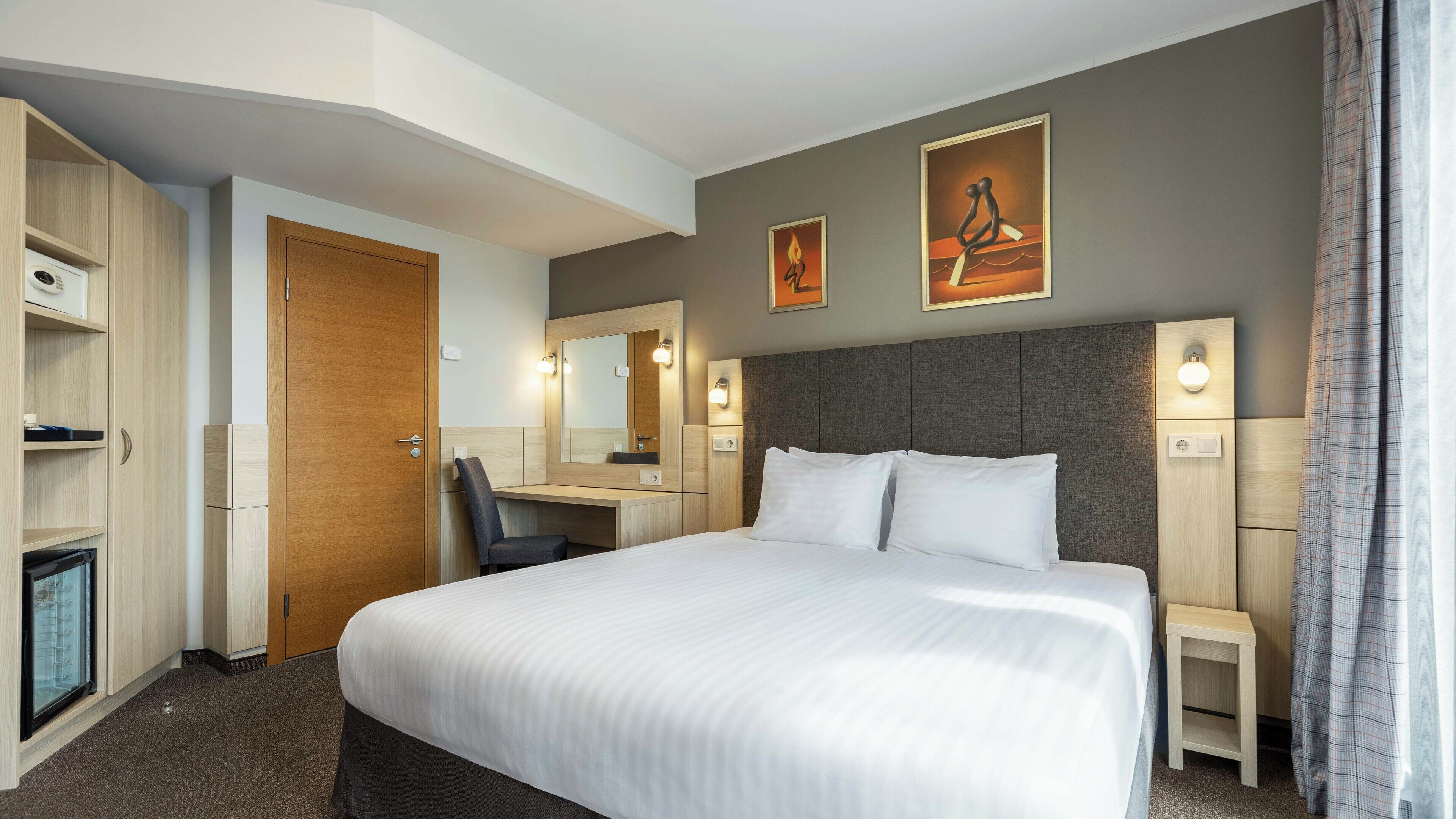 Quarto de hotel com cama grande, escrivaninha, cadeira, guarda-roupa e banheiro.