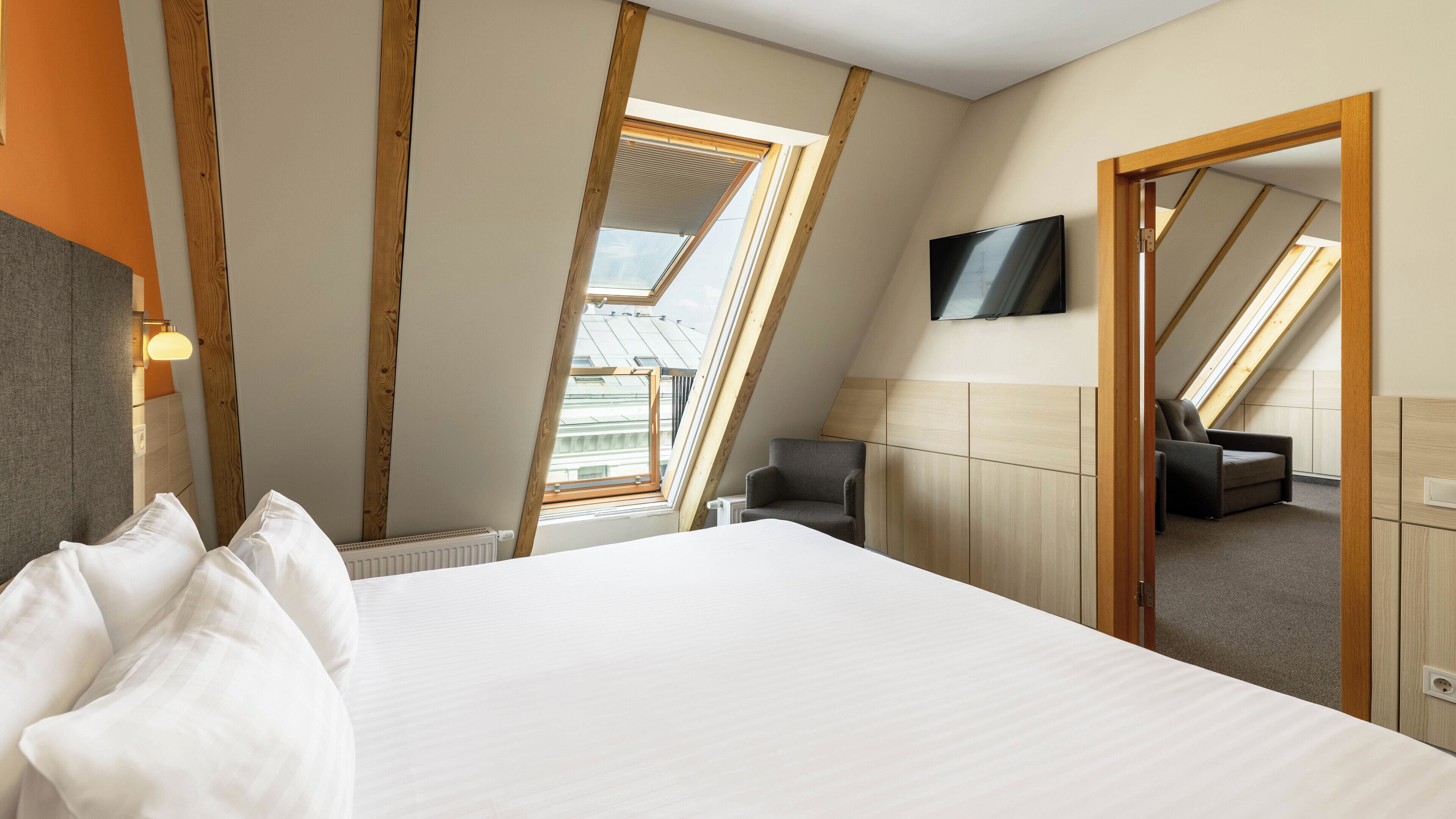 A bedroom with a large bed, a TV mounted on the wall, and a skylight.