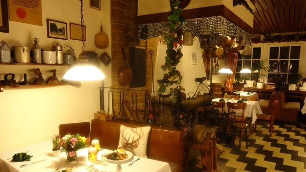 A dining area with tables set for meals, a fireplace, and various kitchen utensils on the wall. - Hotel Bürgerbräu (Osnabrueck)