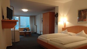 A hotel room with a bed, a desk, a chair, a wardrobe, and a window with a view. - Hotel Bürgerbräu (Osnabrueck)
