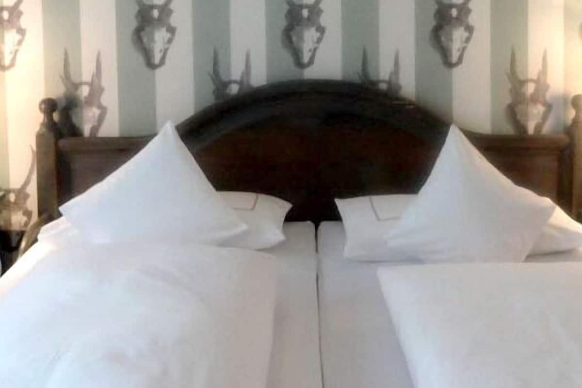 Un lit recouvert de draps blancs dans une pièce dont le papier peint est à rayures et où des crânes d’animaux sont accrochés au mur.