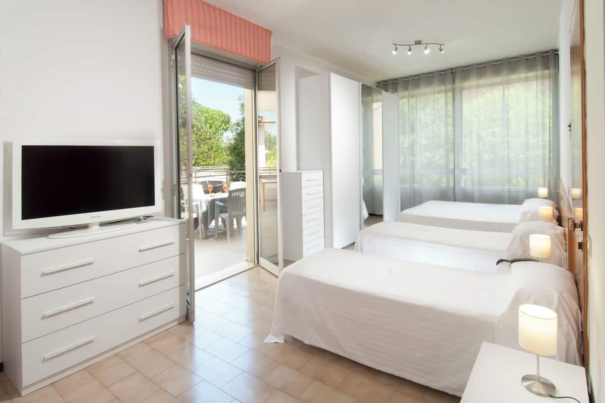 A hotel room with a TV, two beds, a desk with a lamp, and a sliding door to an outdoor area.