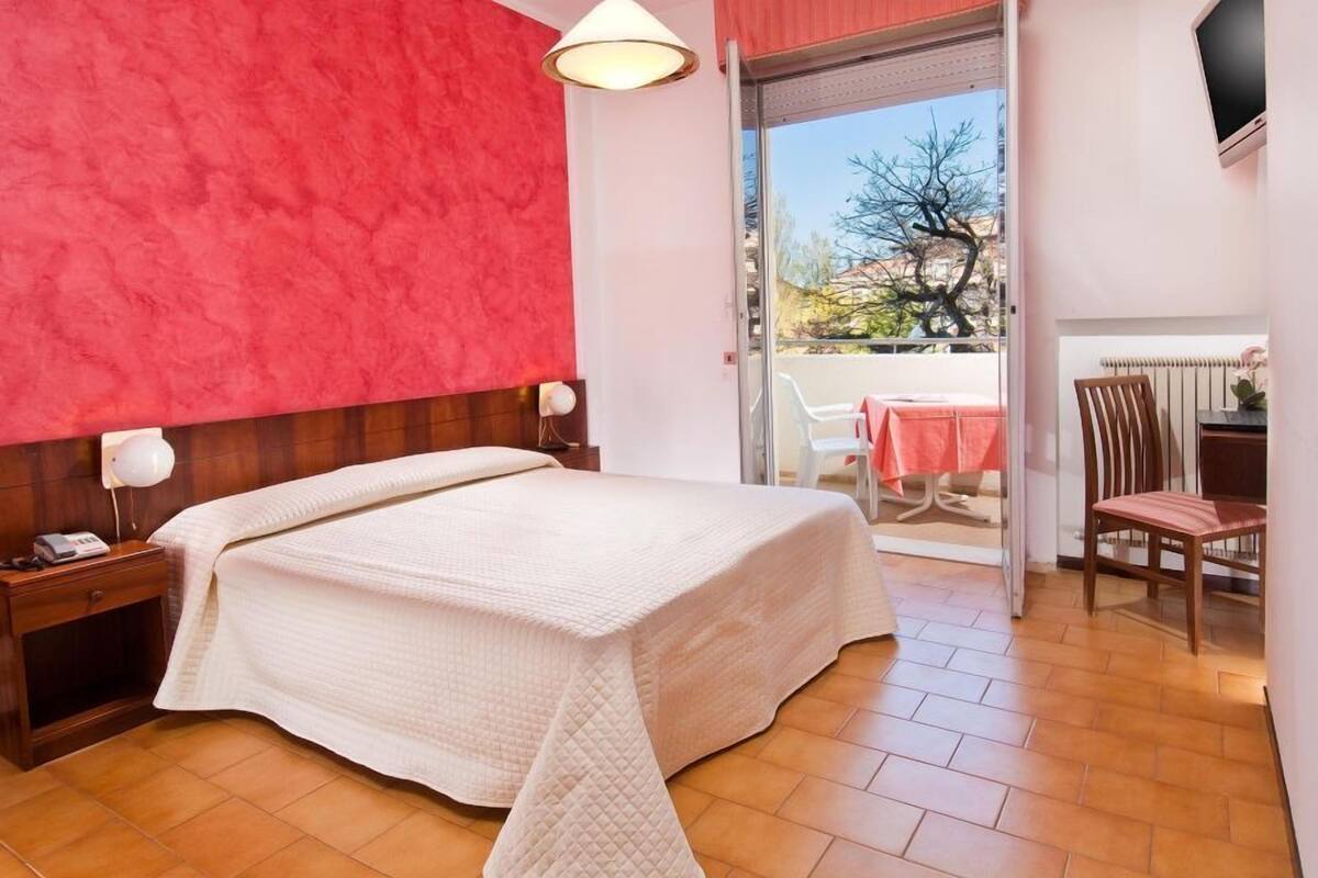 A bedroom with a bed, bedside tables, a lamp, a sliding glass door leading to an outdoor area with a table and chairs.