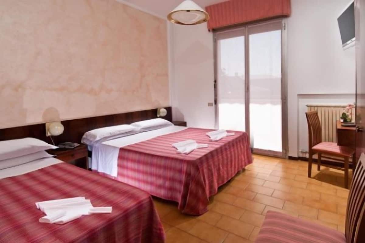 A hotel room with two beds, a chair, a desk, and a large window.