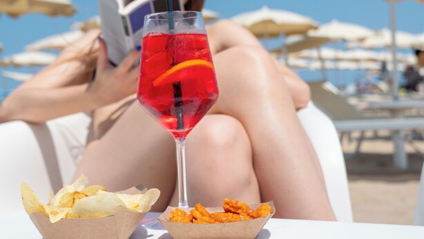 Una persona descansando en una silla de playa con una bebida y aperitivos.