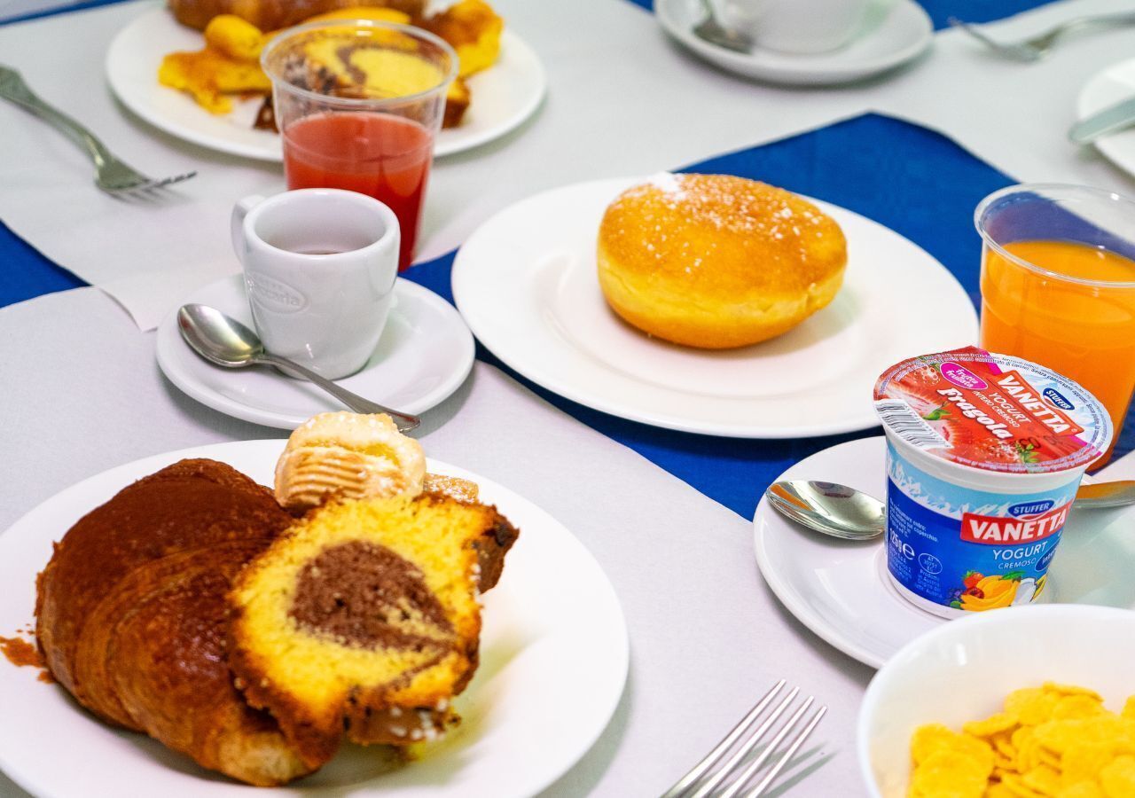 En frukostuppläggning med en croissant, en munk och en kopp yoghurt.