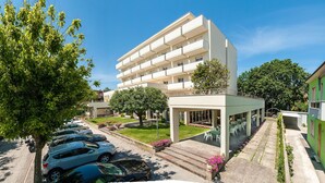 Un hotel moderno de varios pisos, con techo plano, zona de estar cubierta al aire libre y un estacionamiento con varios coches.