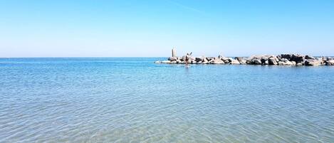 A clear view of a calm sea with a rocky shoreline and a lighthouse in the distance.