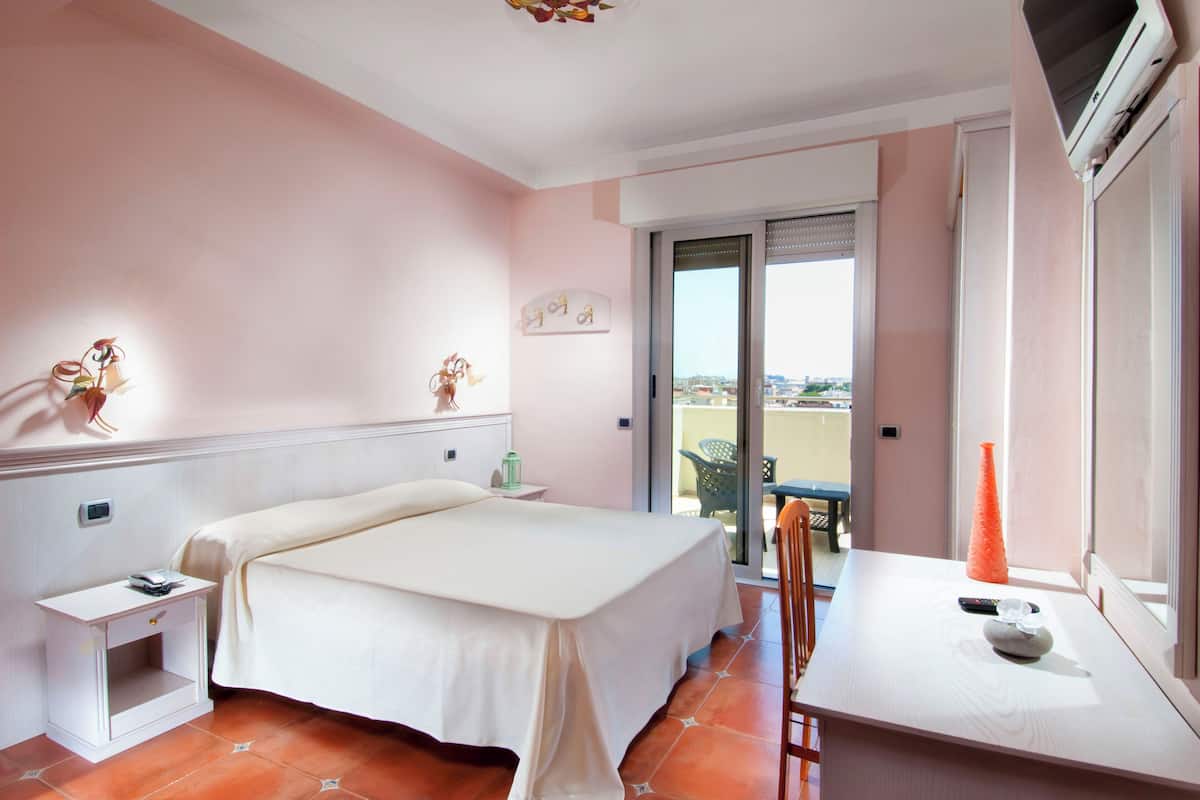 A hotel room with a bed, bedside table, and a small table with a vase and remote control.