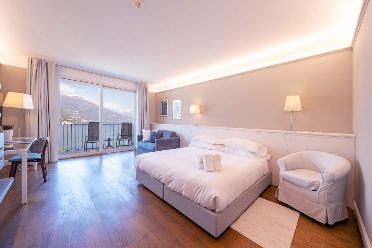 A hotel room with a bed, a chair, a desk, and a balcony with a view.