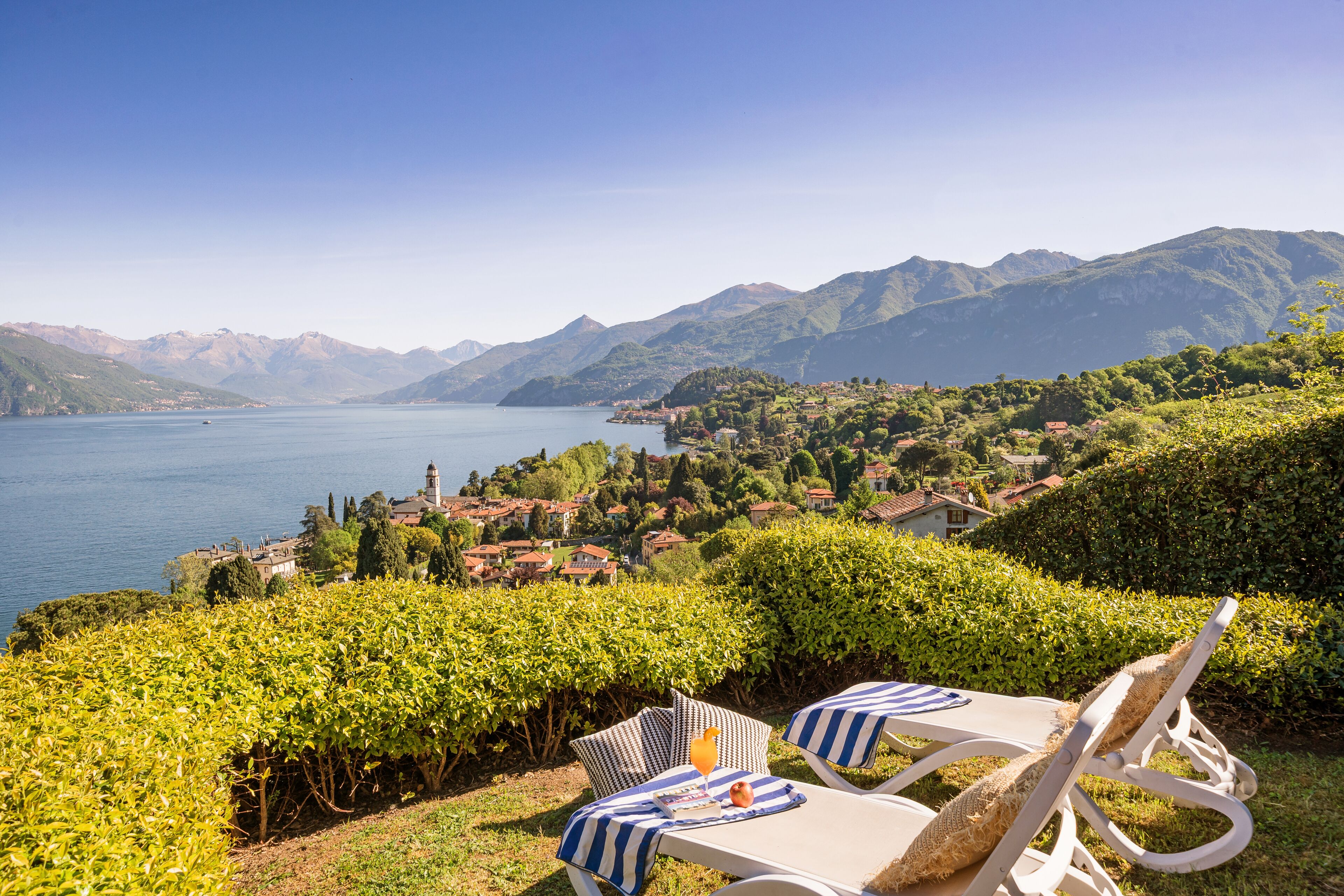 A lakeside view with a vineyard, a table with a chair, and a distant town.