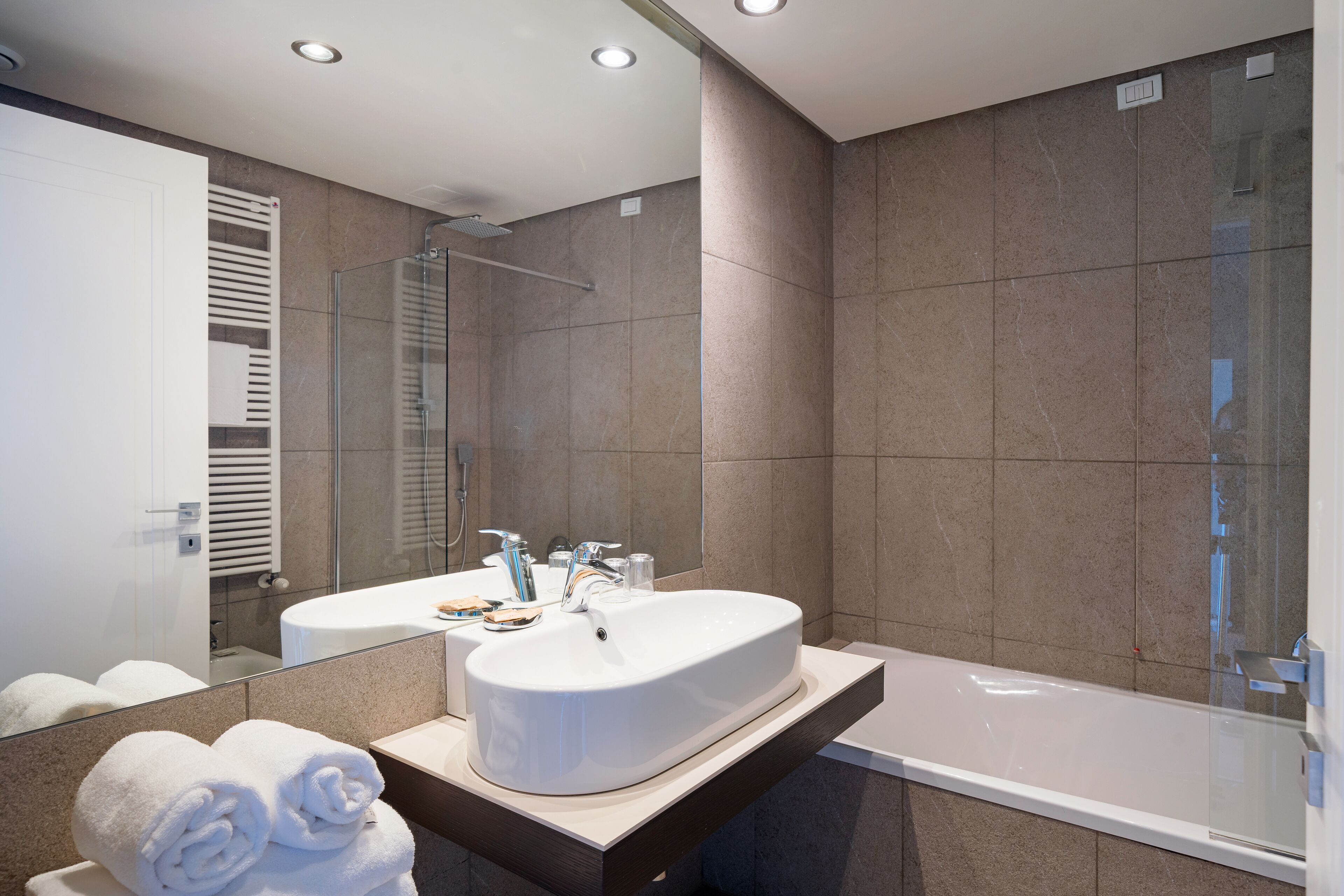 A modern bathroom with a large sink, a glass shower enclosure, and a vanity with towels.