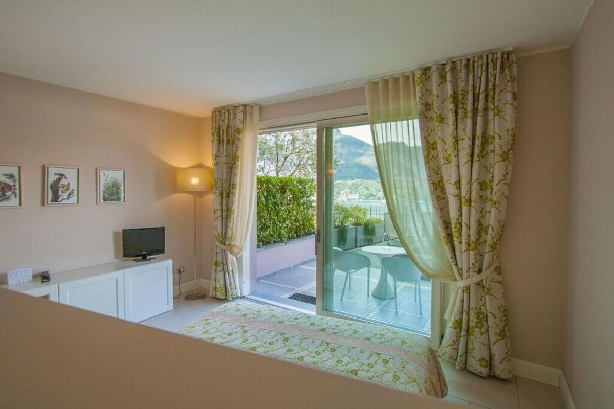 A bedroom with a balcony, a television on a cabinet, and framed pictures on the wall.