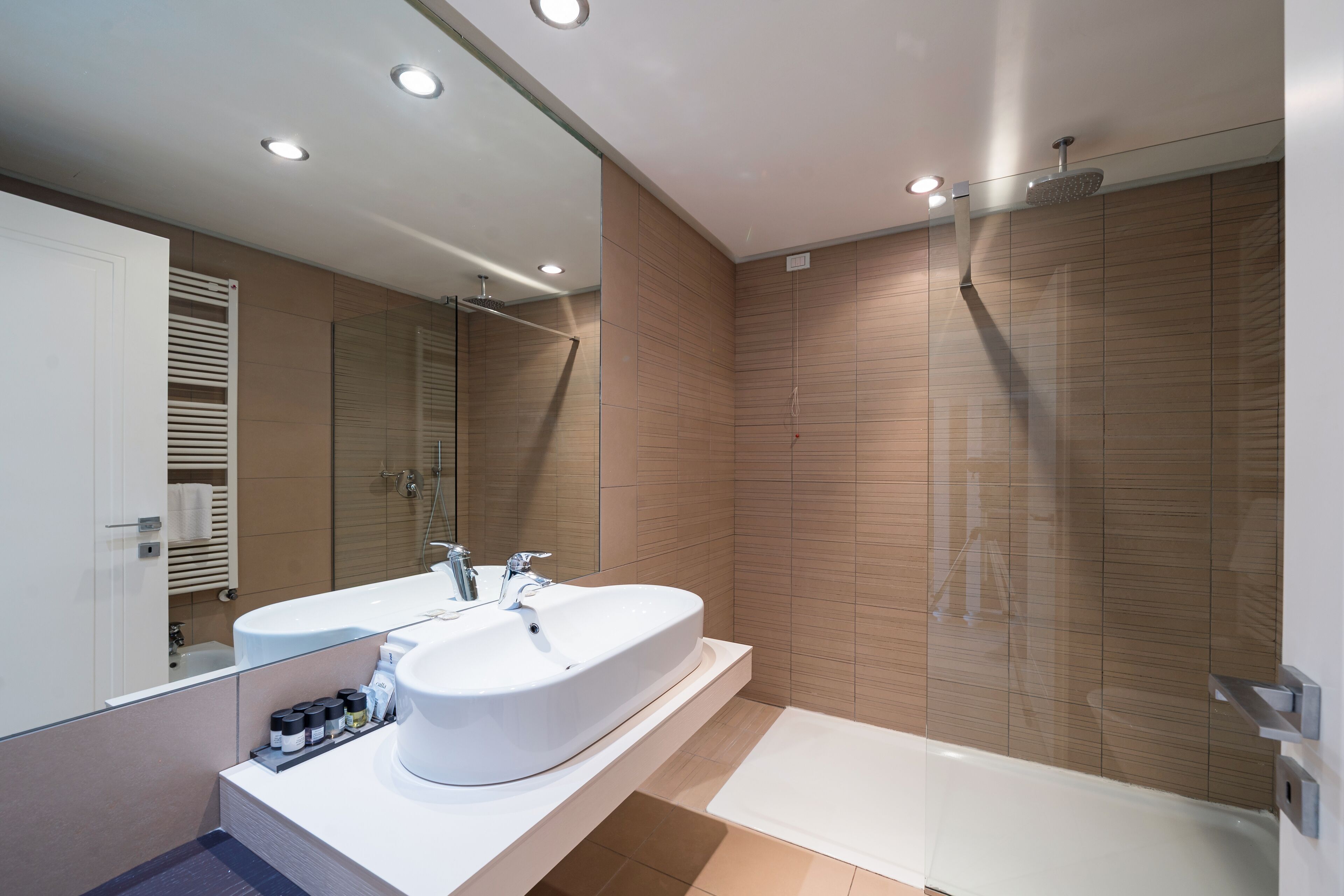 A modern bathroom with a large white sink, a shower, and a mirror.