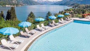 Zona junto a la piscina con sillones y sombrillas, con vista a un lago y montañas al fondo.
