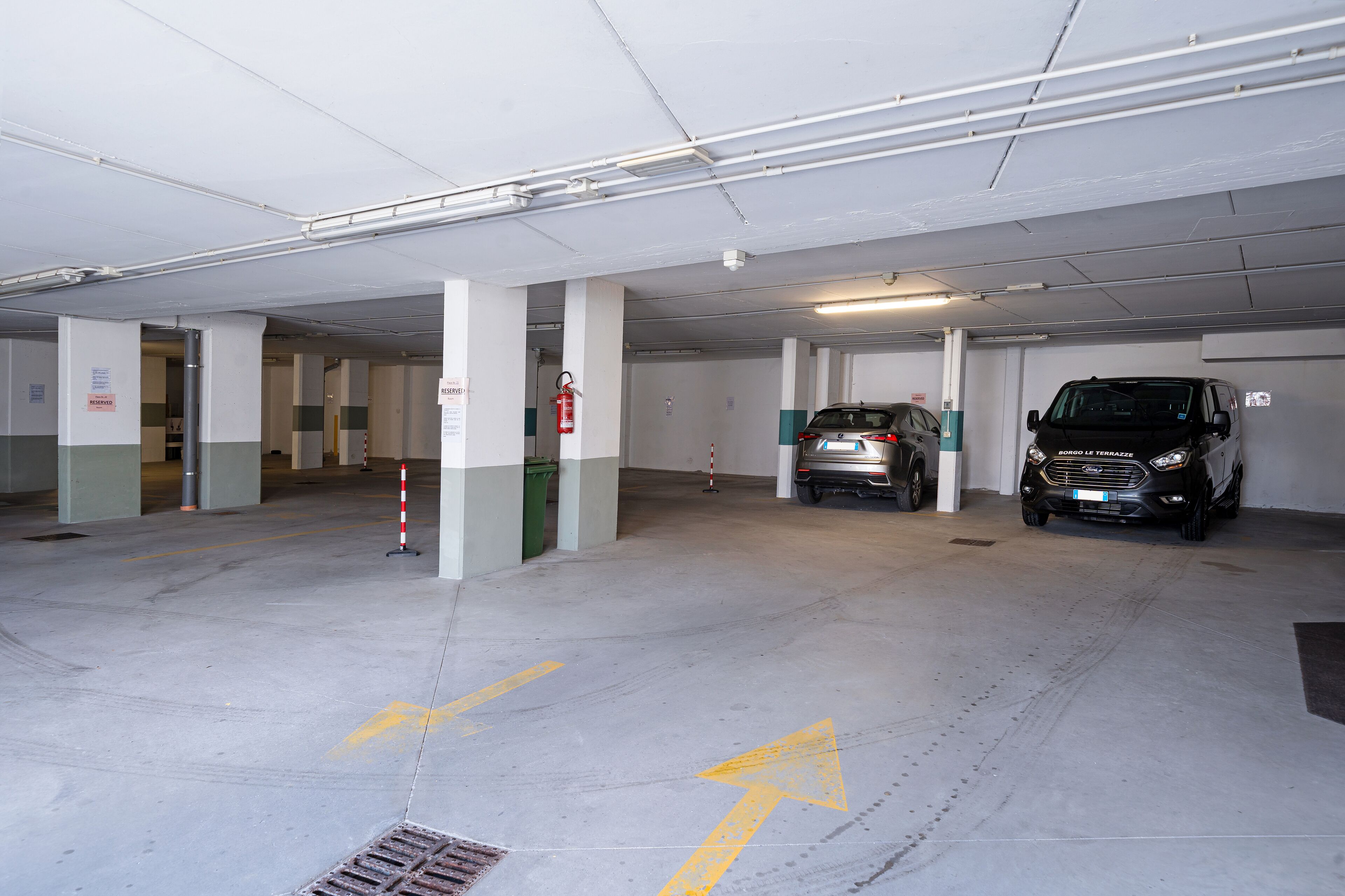 A multi-level parking garage with cars parked on different levels, visible structural columns, and directional arrows on the floor.