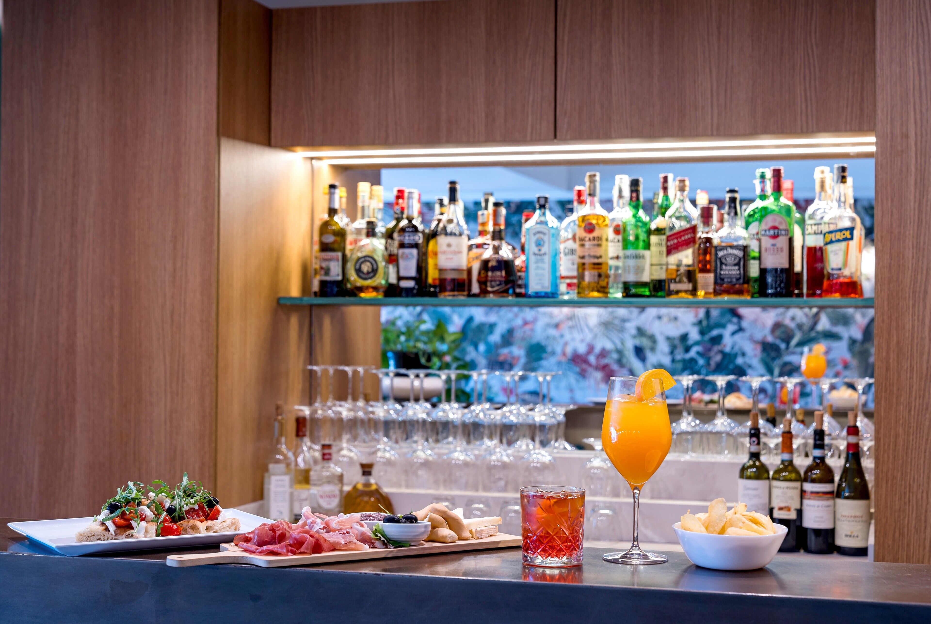 A bar area with a variety of liquor bottles, glasses, and a selection of food and drinks on the counter.