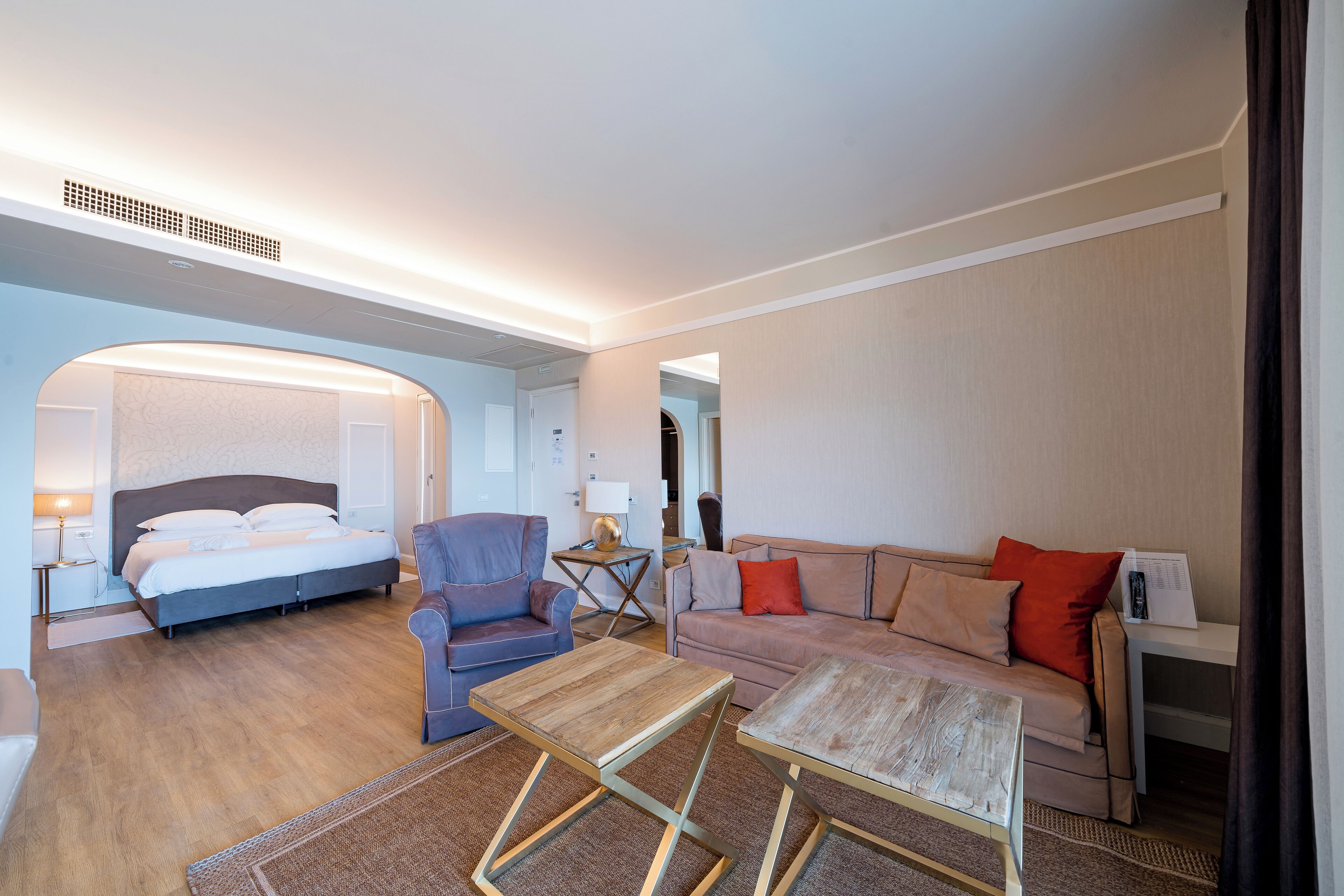 A hotel room with a bed, two sofas, a coffee table, and a desk with a lamp.