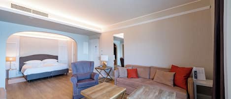 A hotel room with a bed, two sofas, a coffee table, and a desk with a lamp.