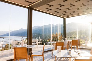 Un'elegante zona pranzo con tavoli e sedie, ampie finestre con vista sulle montagne e una ringhiera in vetro che si affaccia su un lago.