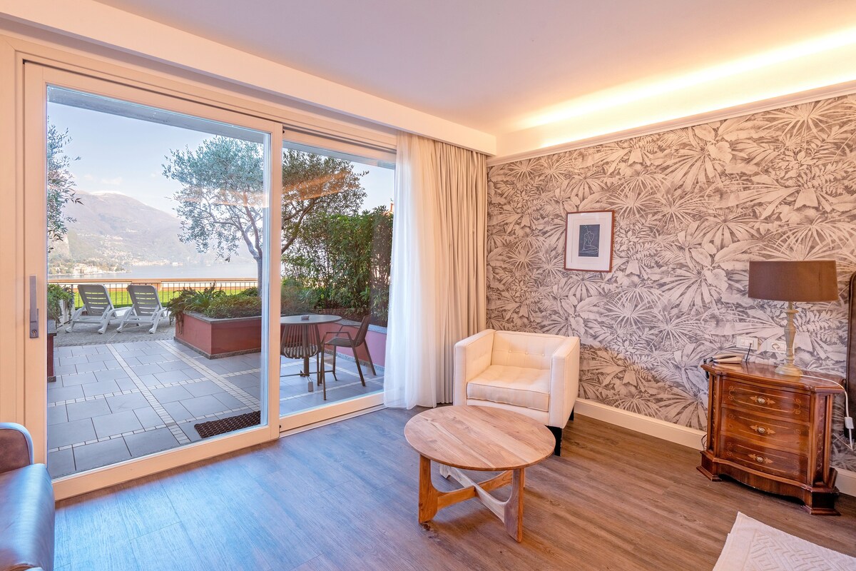 A room with a sliding glass door to an outdoor patio, a white armchair, a wooden coffee table, and a patterned wallpaper.