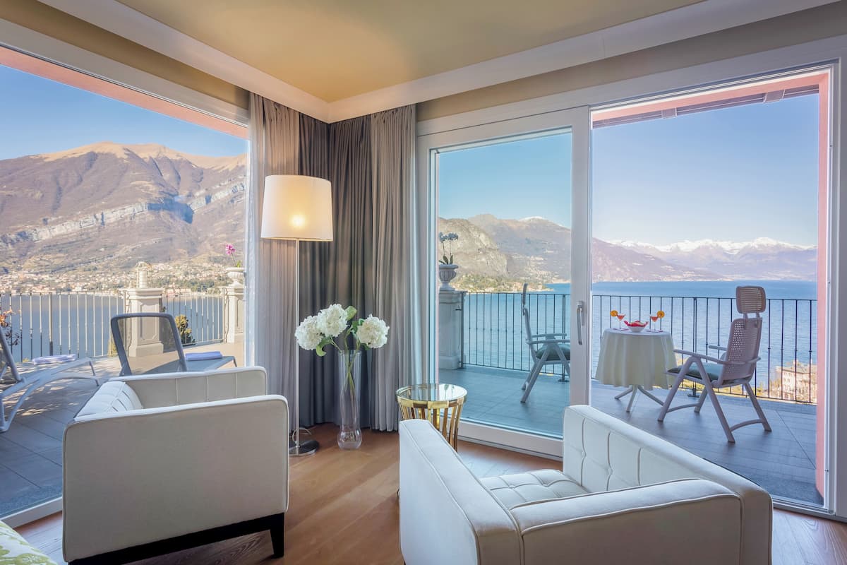 A modern hotel room with a balcony, a sofa, a small table, and a vase of flowers.