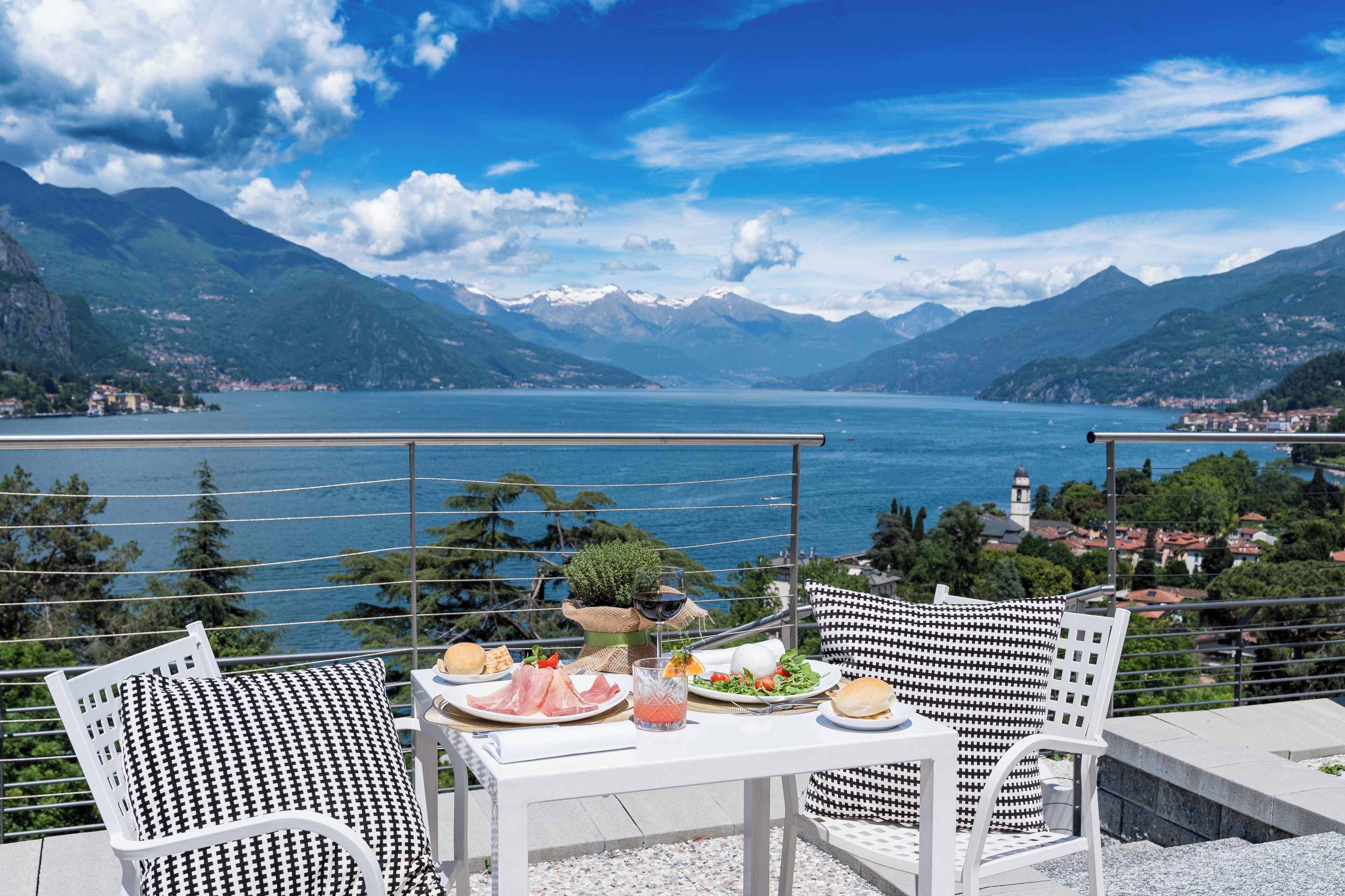 A terrace with a table set for a meal, overlooking a lake and mountains.