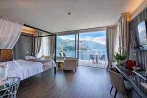 Una camera d'hotel con un letto grande, una zona relax con vista sulle montagne e un balcone con tavolo e sedie.