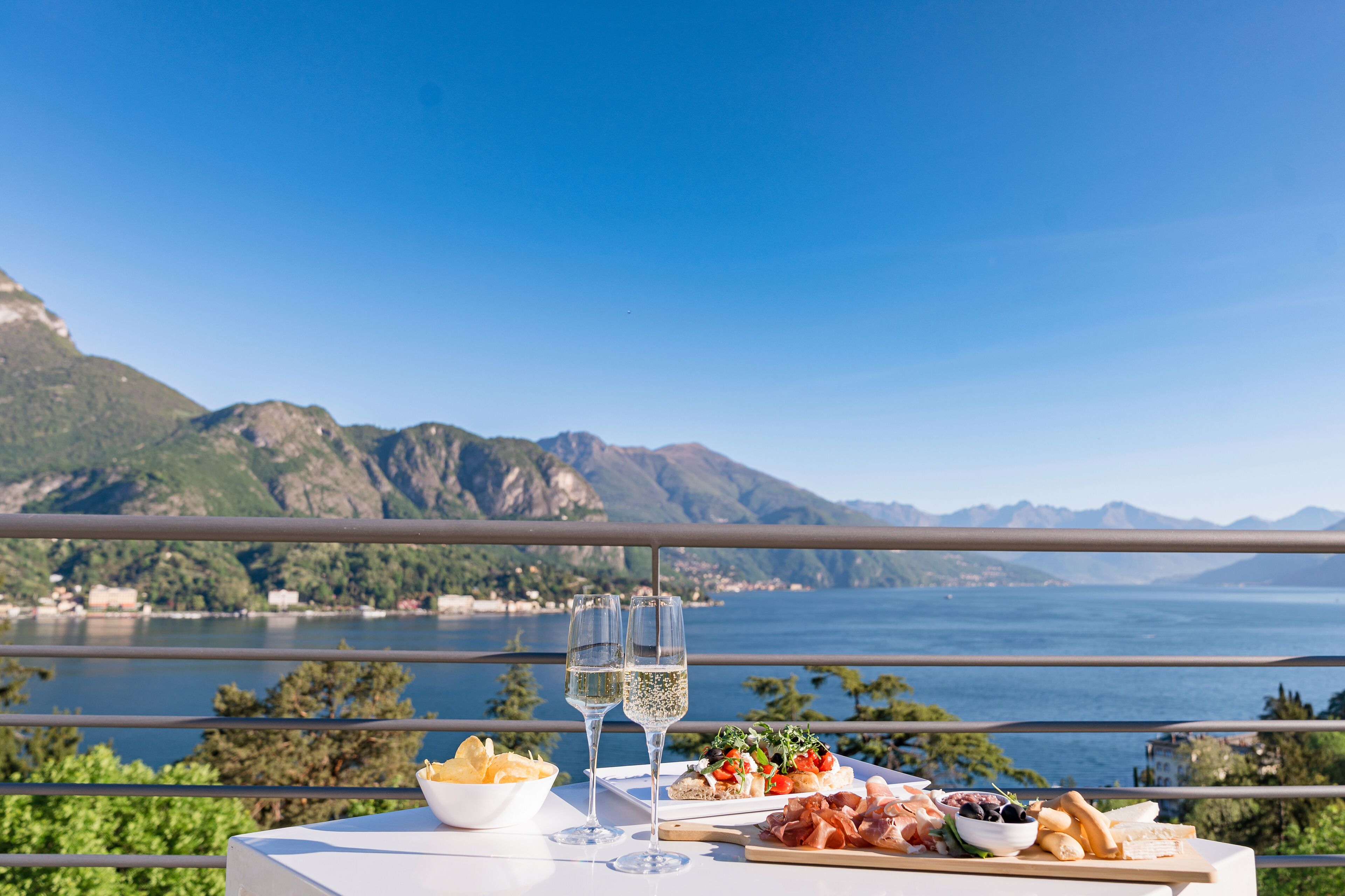 A table with food and drinks, a view of a lake and mountains.