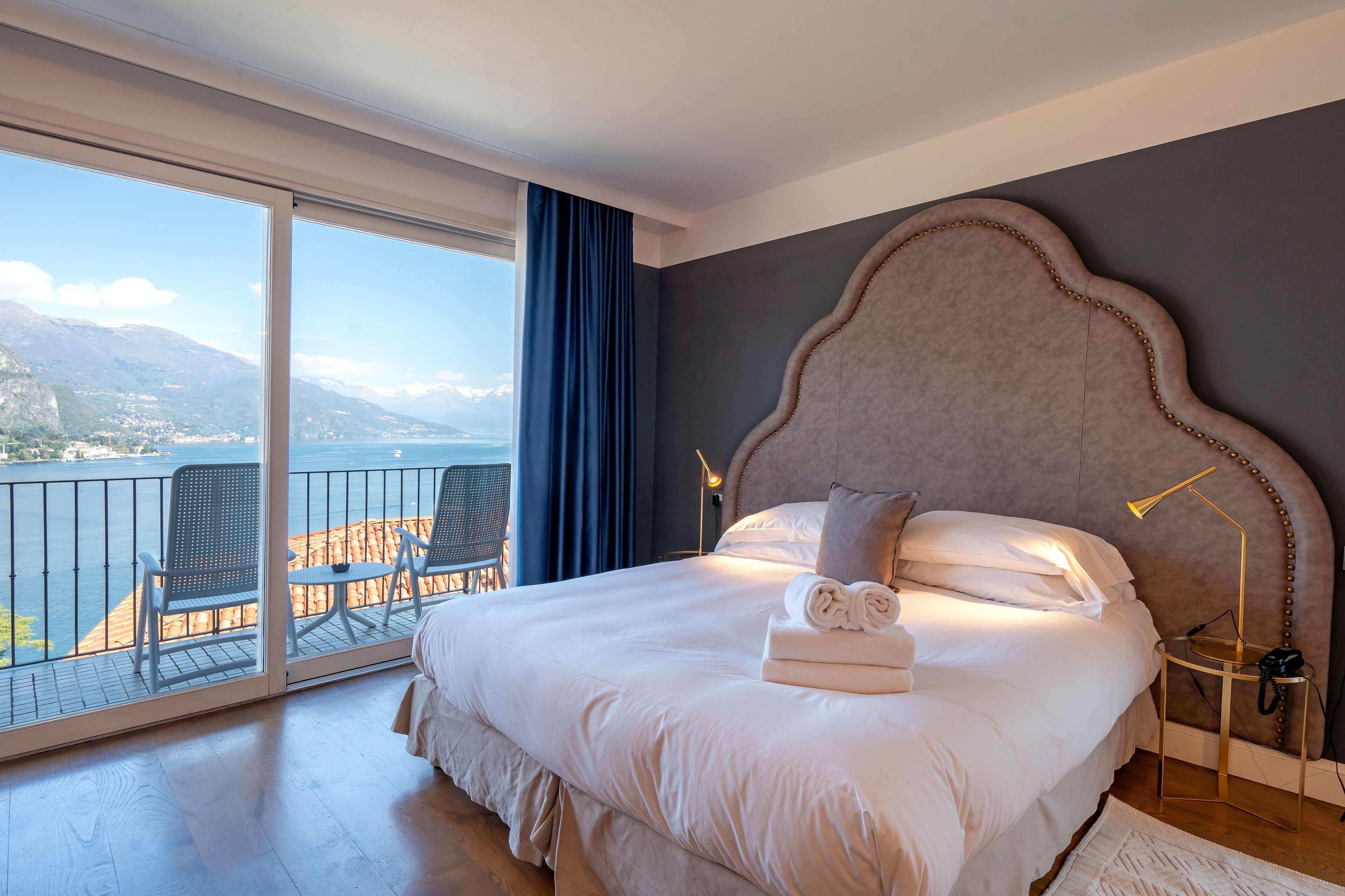 Une chambre avec un grand lit, une vue sur la mer et un balcon équipé de chaises.