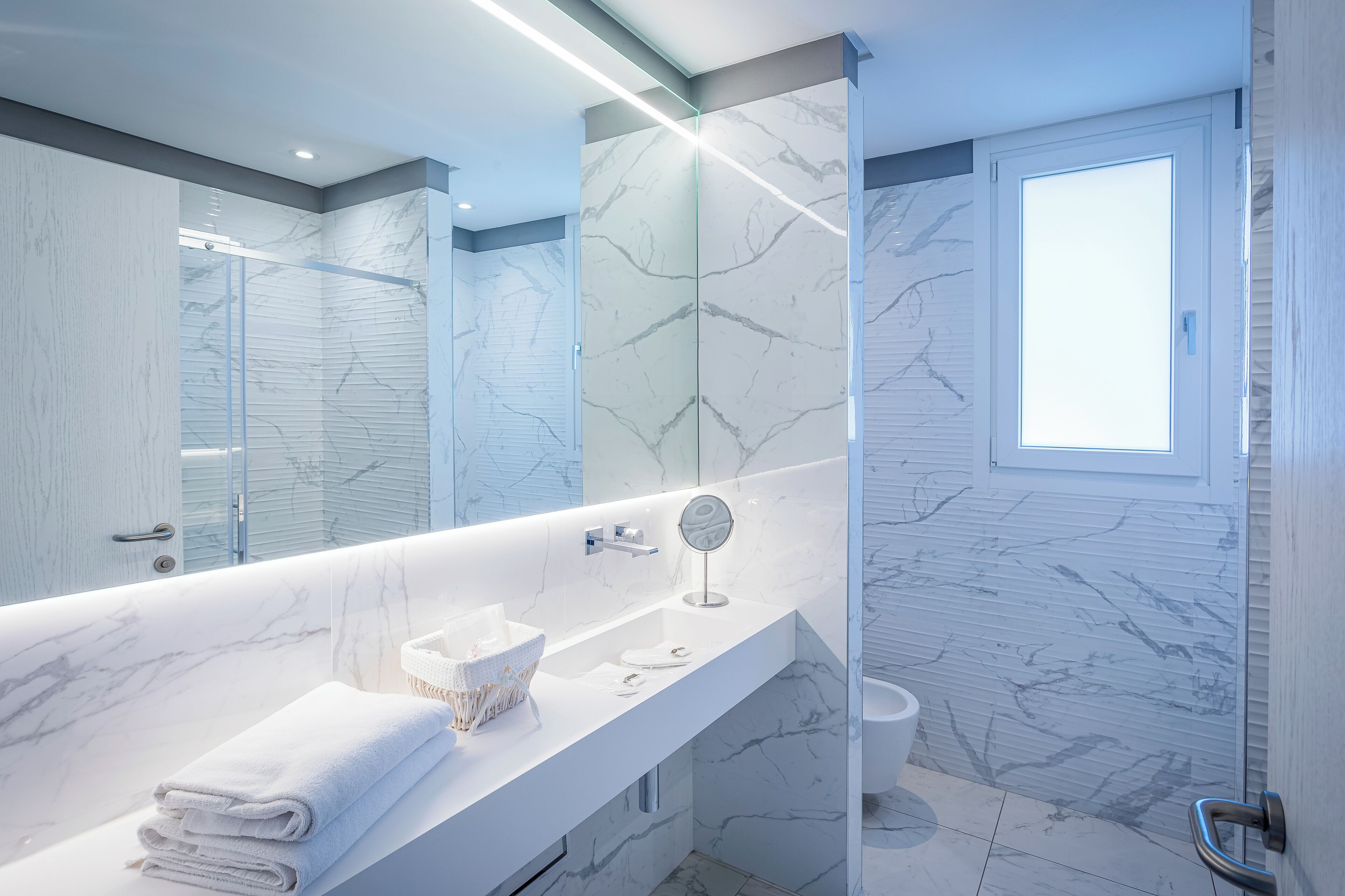 A modern bathroom with a marble vanity, a glass shower enclosure, and a large mirror.