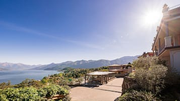 Un hotel frente al mar con terraza y vistas al océano, con montañas al fondo y cielo despejado.