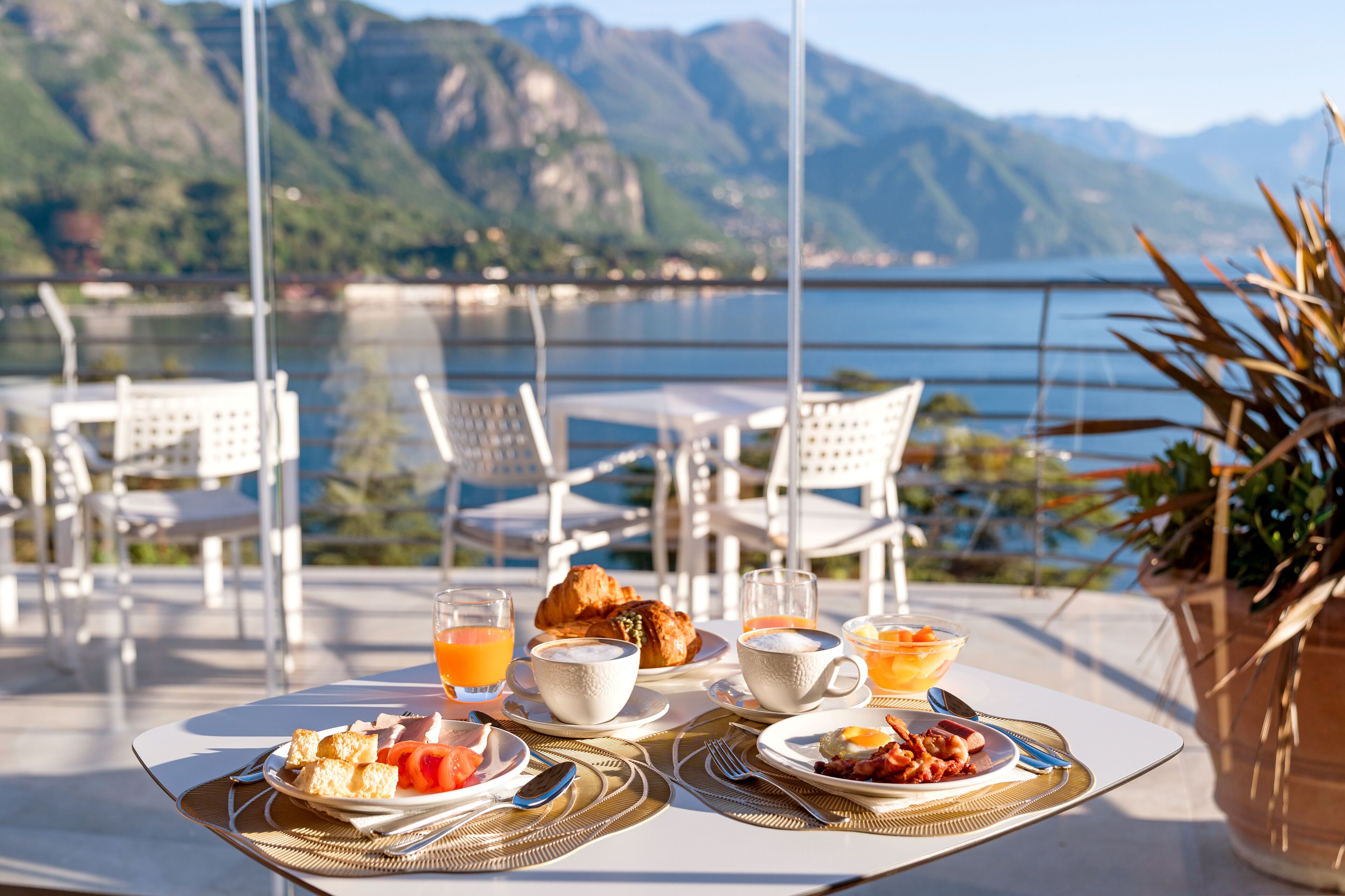 Ein Esstisch mit Croissants, Obst und Getränken mit Blick auf einen Bergsee.