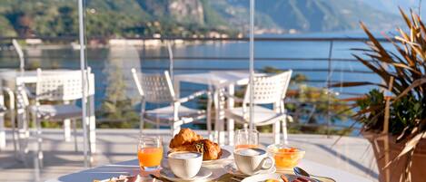 Ein Esstisch mit Croissants, Obst und Getränken mit Blick auf einen Bergsee.