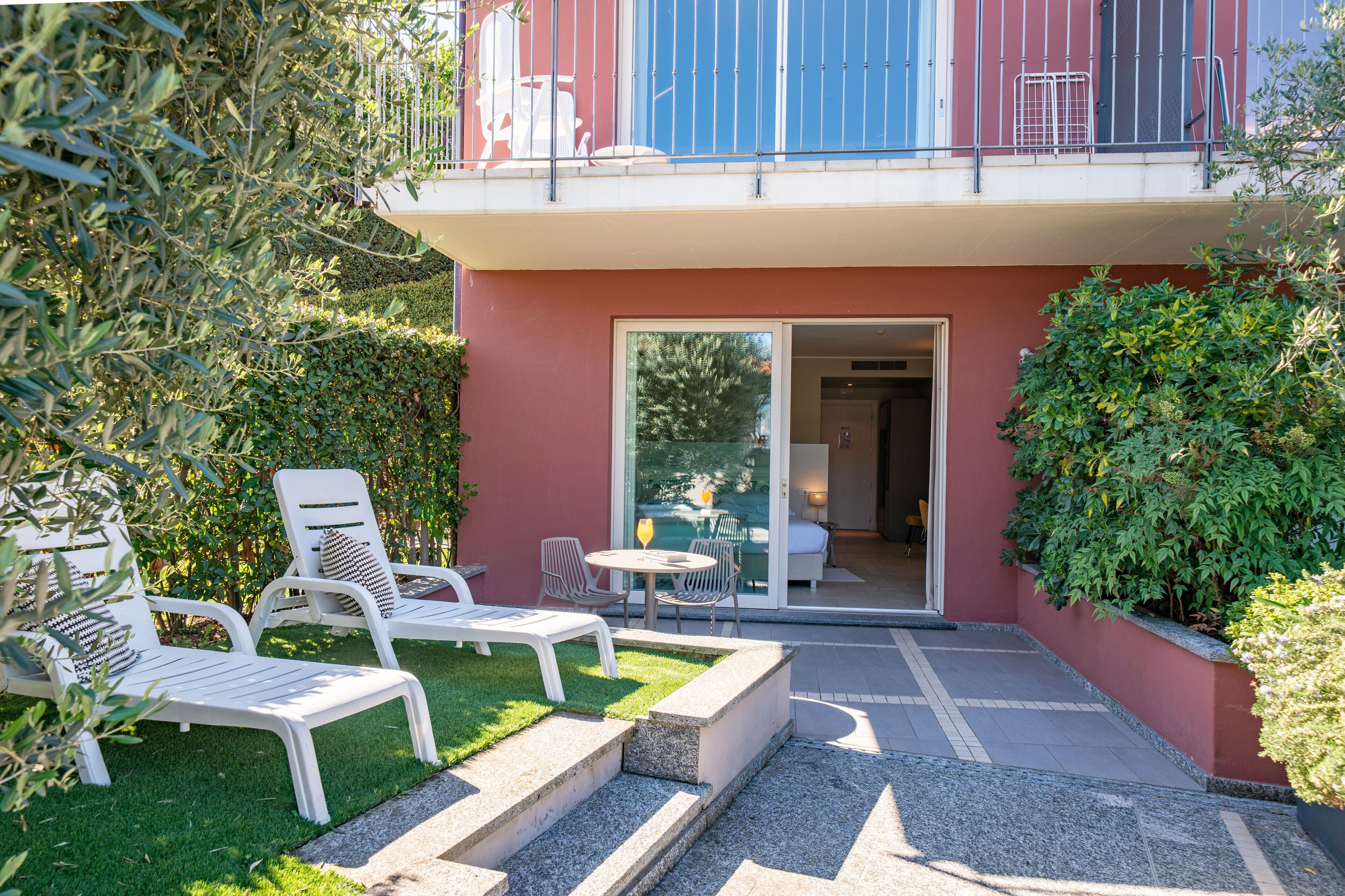 Ein Balkon mit weißen Geländern, eine kleine Sitzgelegenheit im Freien mit weißen Stühlen und einem Tisch sowie eine Glastür zu einem Innenbereich.