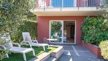 Ein Balkon mit weißen Geländern, eine kleine Sitzgelegenheit im Freien mit weißen Stühlen und einem Tisch sowie eine Glastür zu einem Innenbereich.