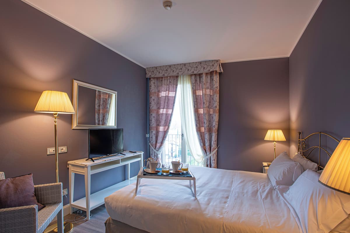 A hotel room with a bed, bedside lamps, a desk with a television, and a window with curtains.