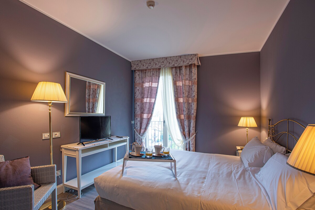 Una habitación de hotel con cama, lámparas de noche, escritorio y televisor, además de una ventana con cortinas.