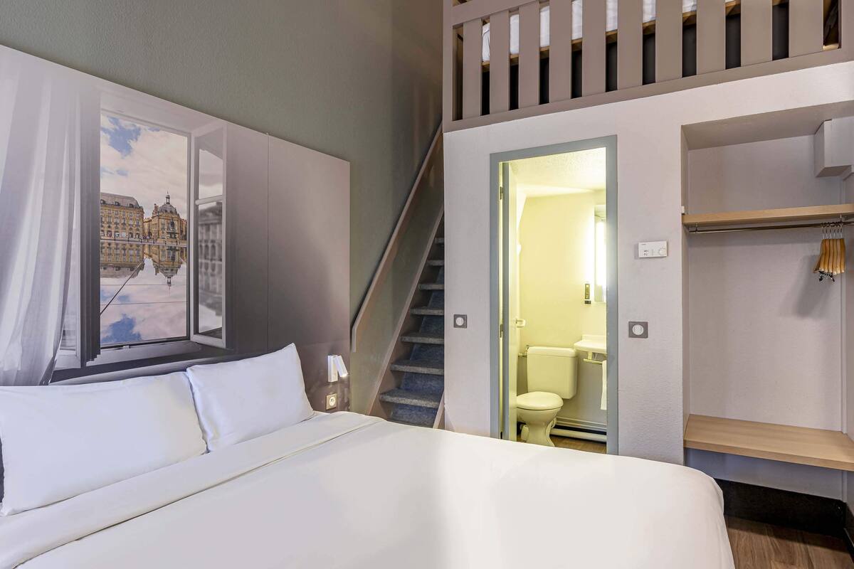 Ein Hotelzimmer mit Bett, einem Gemälde eines Gebäudes, einer Treppe und einem Badezimmer.