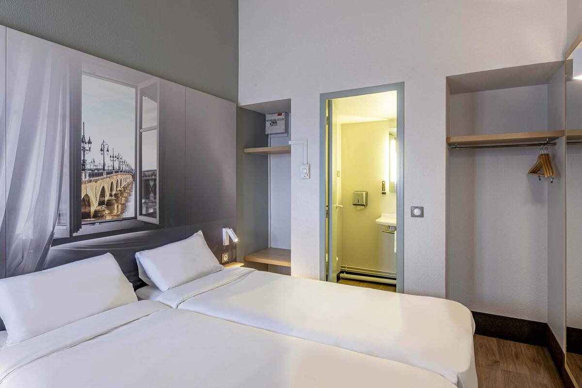 Ein Hotelzimmer mit einem großen Bett, einem Fenster mit Blick auf eine Brücke, einem Badezimmer mit Dusche und einem Holzregal mit Kleiderhaken.