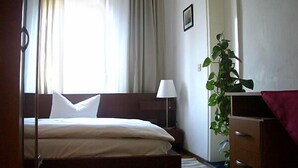 Ein Schlafzimmer mit einem Bett, einem Nachttisch mit Lampe, einer Kommode und einer Zimmerpflanze.
